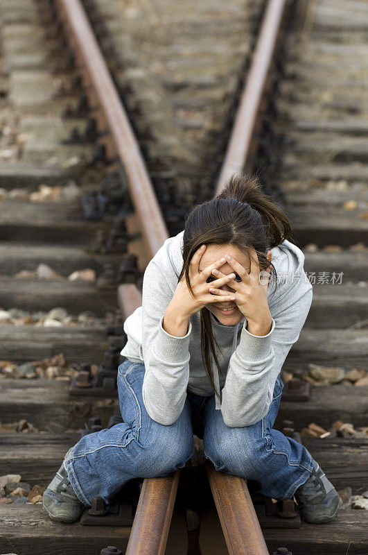 女孩坐在铁轨上， 双手捂着脸